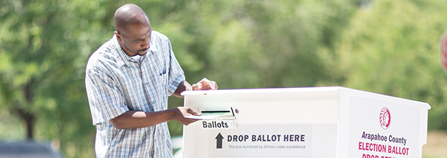 African American male inserts ballot envelope into ballot box