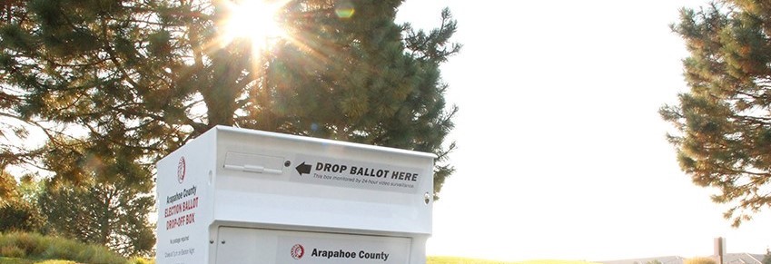 White ballot drop box in front of trees with sunlight streaming through leaves