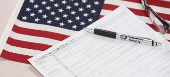 Image of a pen sitting on a voter registration form atop an American flag